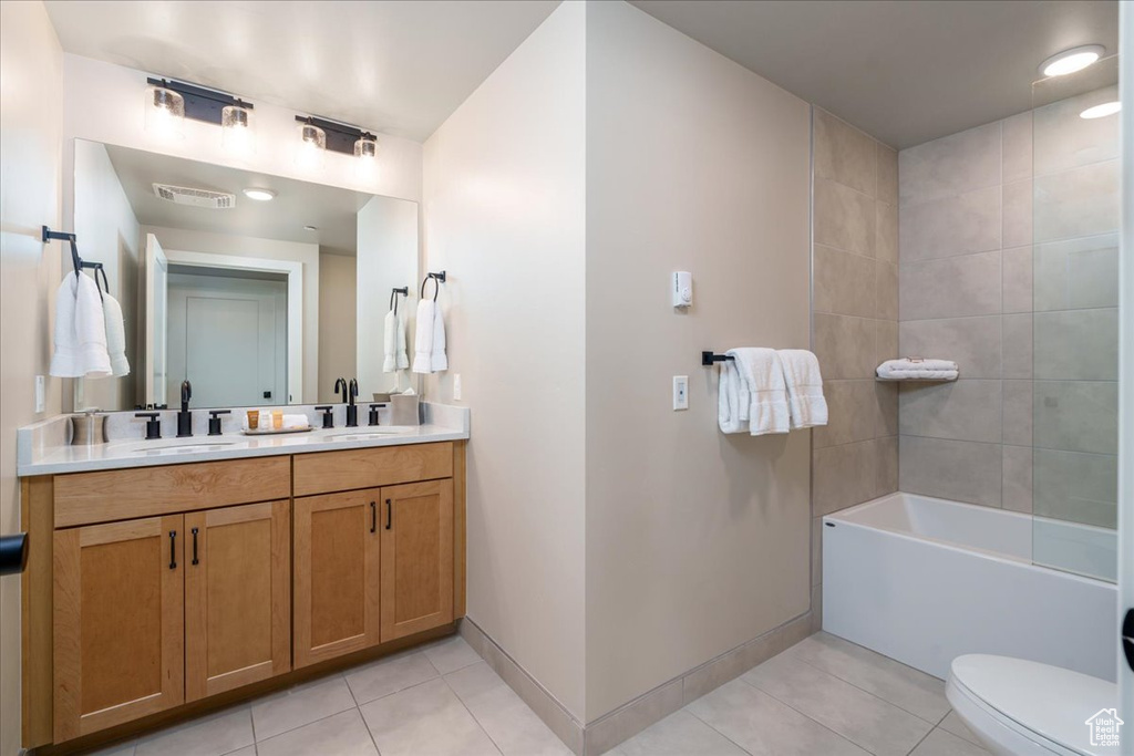 Full bathroom featuring tiled shower / bath combo, double sink vanity, tile flooring, and toilet