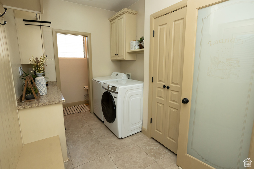 Clothes washing area with cabinets, washer and clothes dryer, light tile floors, and washer hookup