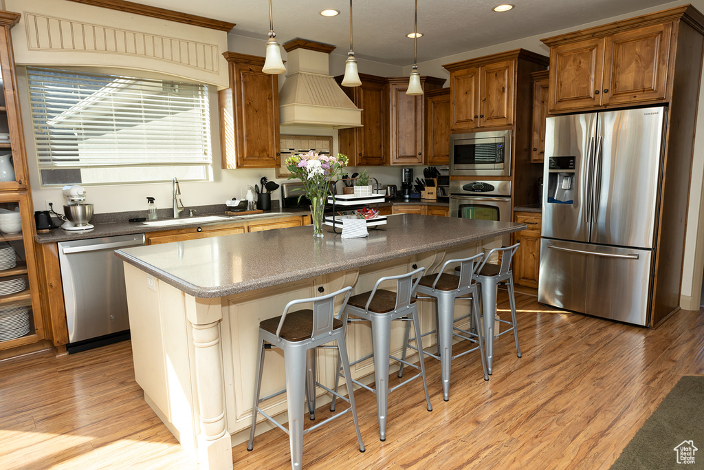 Kitchen featuring light hardwood / wood-style floors, a kitchen island, premium range hood, a breakfast bar, and appliances with stainless steel finishes