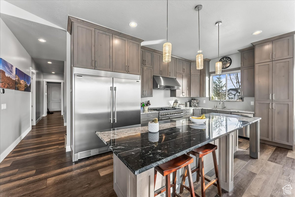 Kitchen with dark hardwood / wood-style flooring, dark stone counters, a breakfast bar, high quality appliances, and a center island