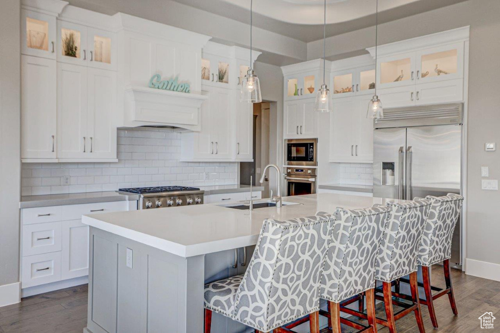 Kitchen with built in appliances, a kitchen breakfast bar, a kitchen island with sink, and decorative light fixtures