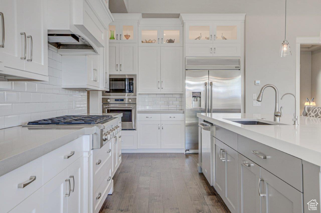 Kitchen featuring custom range hood, tasteful backsplash, sink, stainless steel appliances, and decorative light fixtures