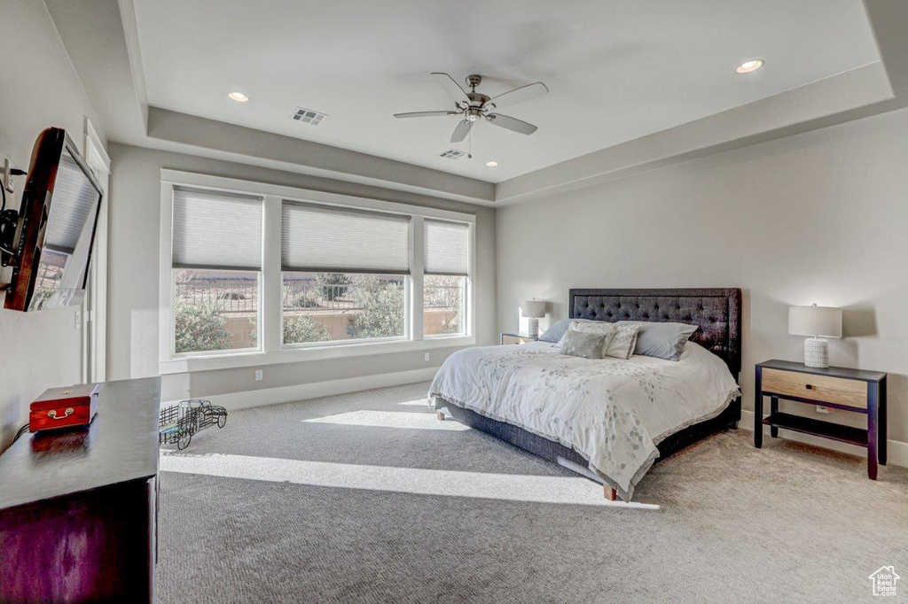 Bedroom featuring light carpet, a raised ceiling, and ceiling fan