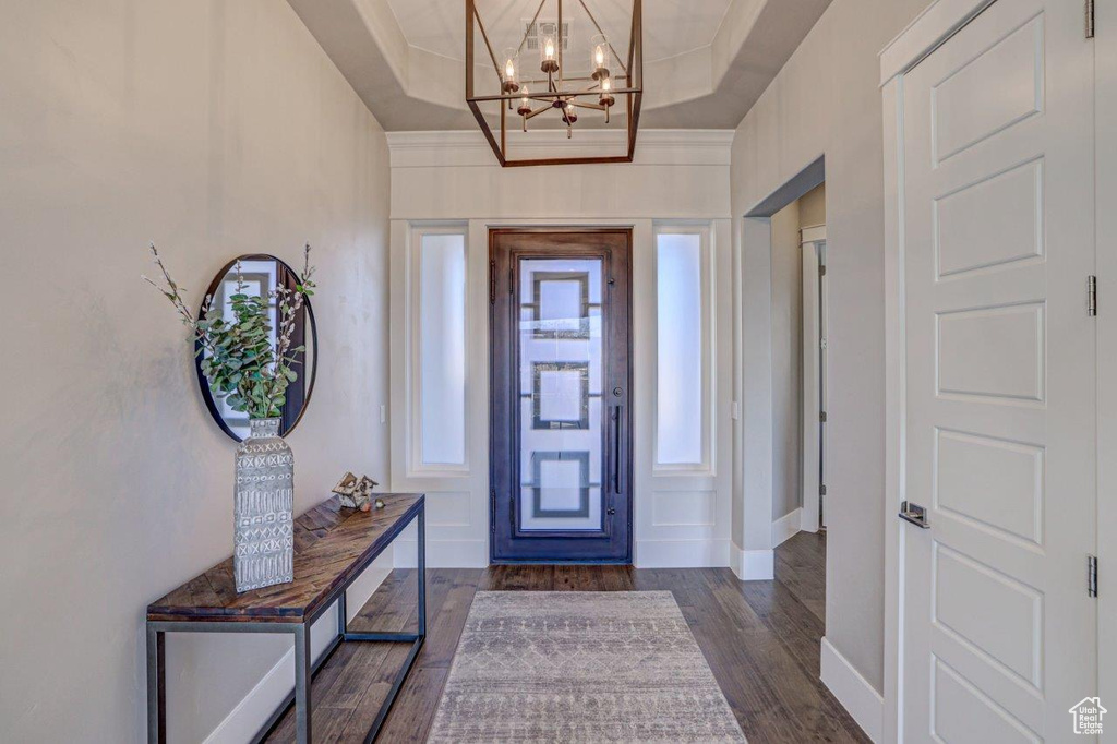 Entryway featuring a tray ceiling, a notable chandelier, crown molding, and dark hardwood / wood-style flooring