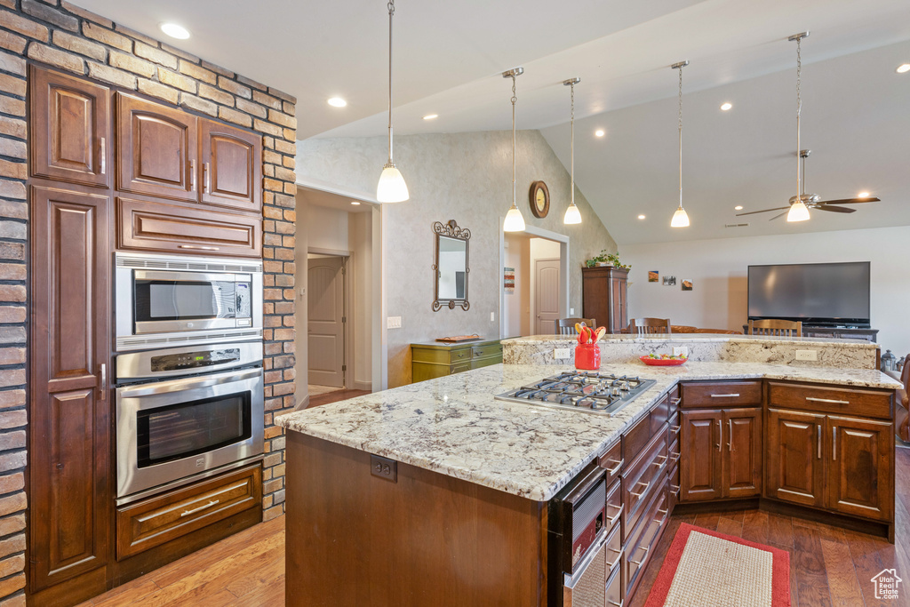 Kitchen featuring dark hardwood / wood-style flooring, light stone counters, appliances with stainless steel finishes, vaulted ceiling, and ceiling fan