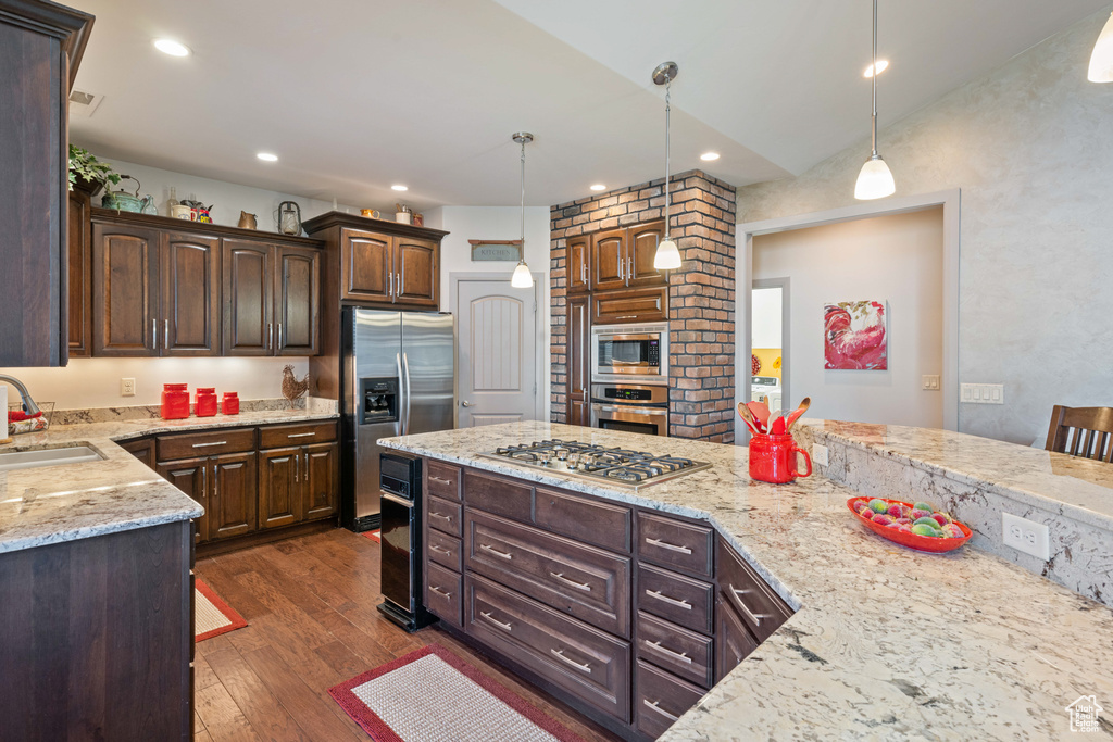Kitchen featuring pendant lighting, appliances with stainless steel finishes, light stone counters, and dark wood-type flooring