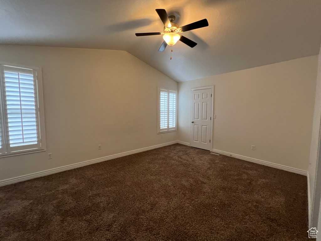 Spare room featuring dark colored carpet, lofted ceiling, and ceiling fan