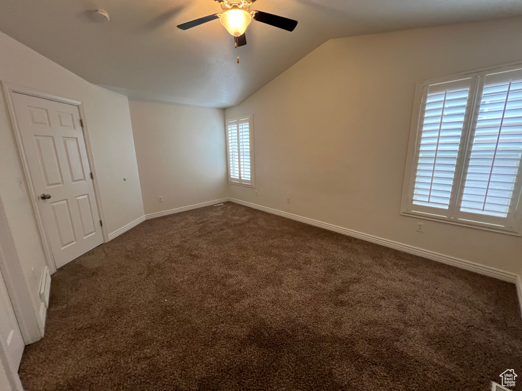 Unfurnished room with dark colored carpet, ceiling fan, and vaulted ceiling