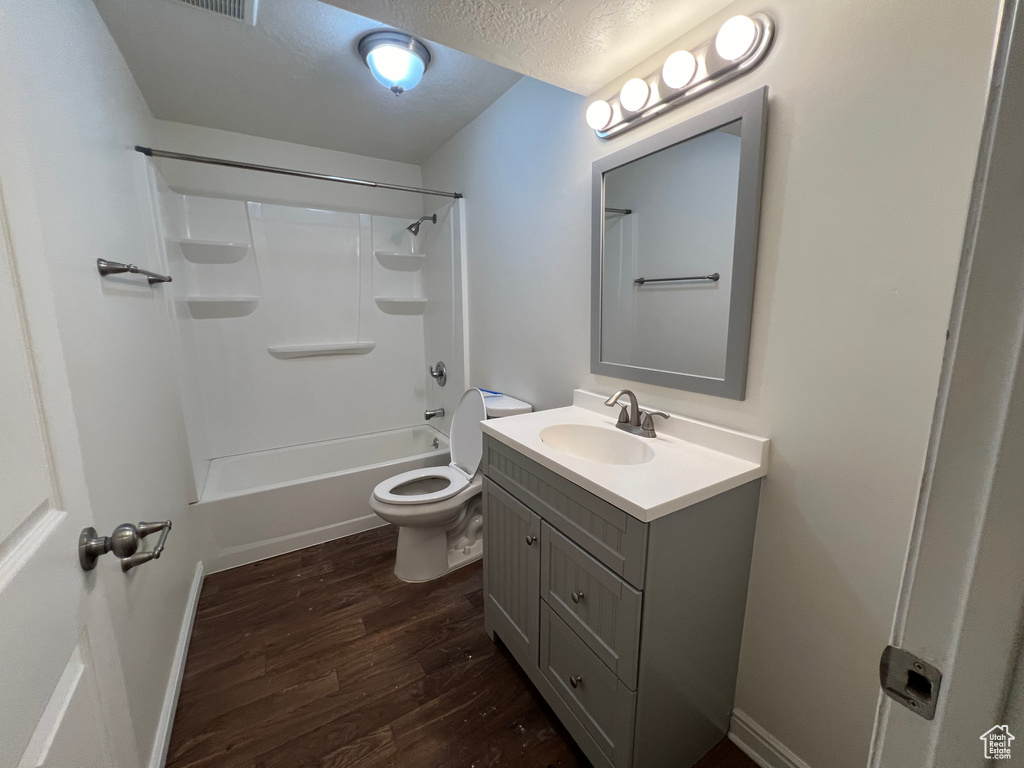 Full bathroom featuring hardwood / wood-style floors, a textured ceiling, toilet, vanity with extensive cabinet space, and shower / bathing tub combination