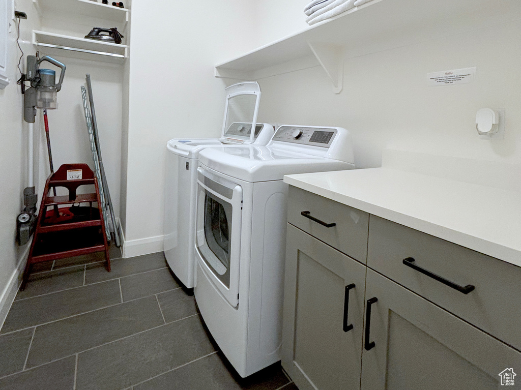 Clothes washing area featuring dark tile floors, cabinets, and washing machine and clothes dryer