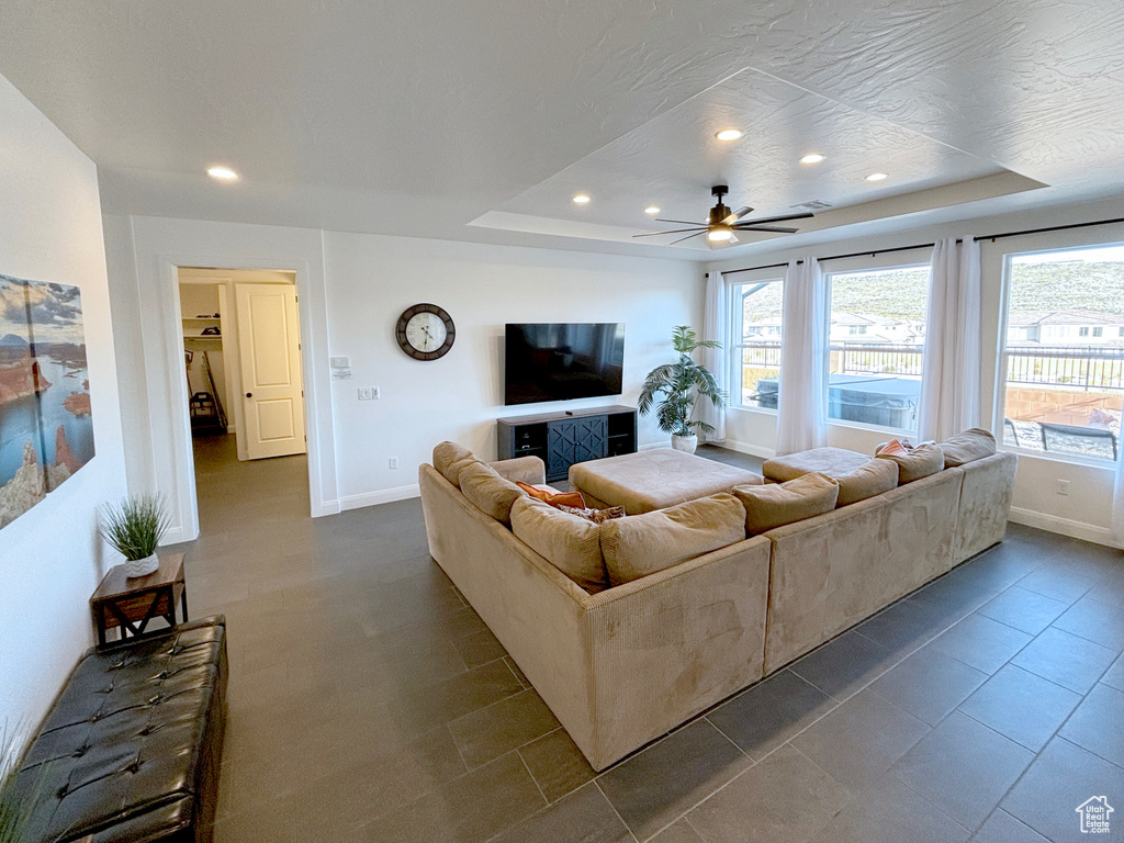 Living room featuring dark tile flooring, ceiling fan, and a raised ceiling