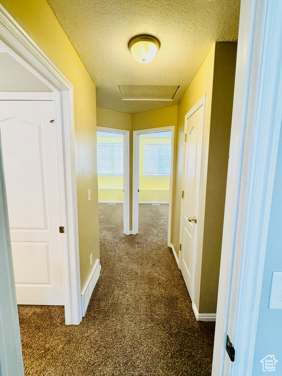 Hallway featuring dark colored carpet and a textured ceiling
