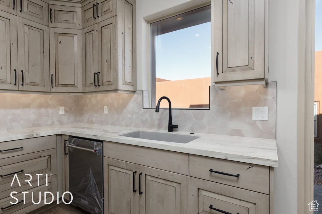 Kitchen with light stone countertops, tasteful backsplash, sink, dishwashing machine, and a healthy amount of sunlight