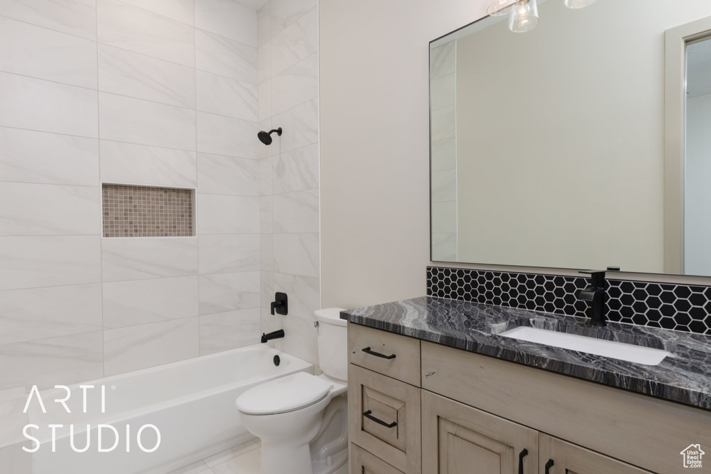 Full bathroom with toilet, vanity with extensive cabinet space, and tiled shower / bath