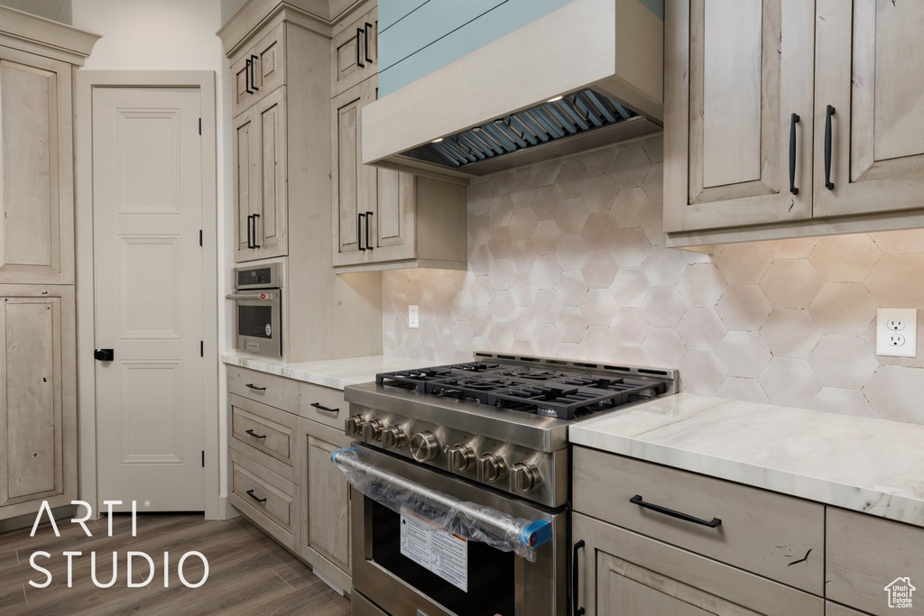 Kitchen featuring backsplash, light stone countertops, dark hardwood / wood-style flooring, premium range hood, and stainless steel stove