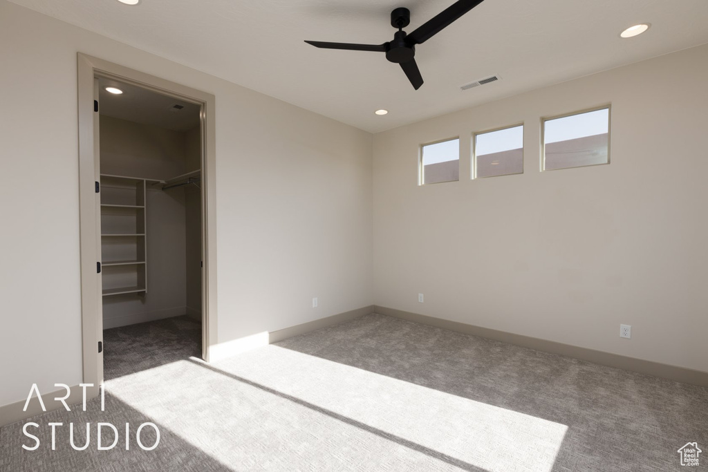 Unfurnished bedroom featuring dark carpet, a spacious closet, and ceiling fan