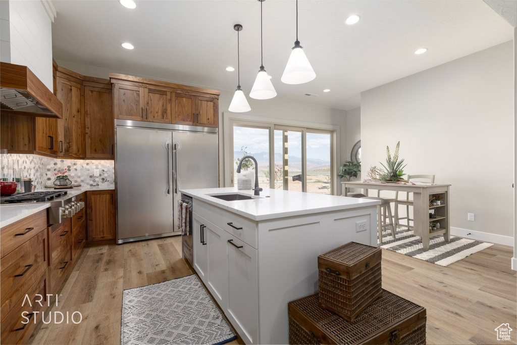 Kitchen featuring light hardwood / wood-style floors, sink, custom exhaust hood, and hanging light fixtures
