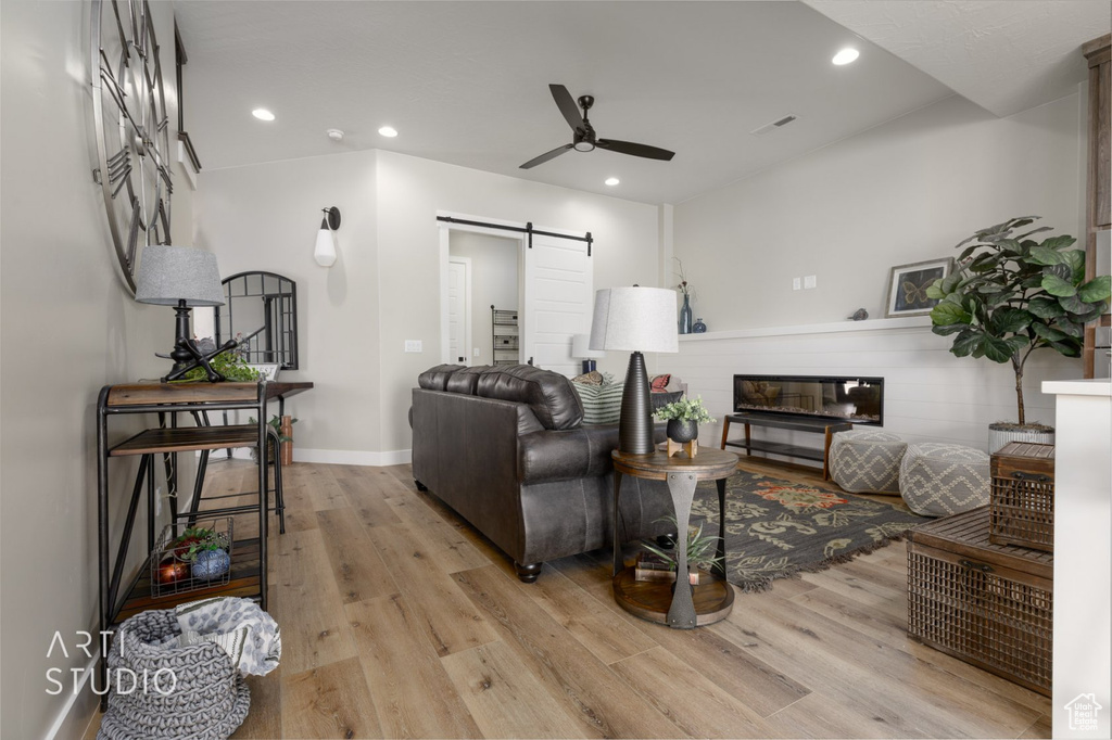 Living room with light hardwood / wood-style floors, ceiling fan, and a barn door