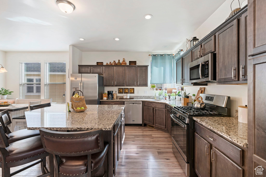 Kitchen featuring light hardwood / wood-style flooring, a kitchen bar, a center island, light stone countertops, and stainless steel appliances