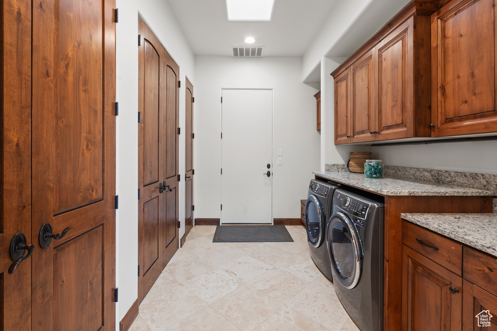Laundry room with light tile floors, washing machine and dryer, and cabinets