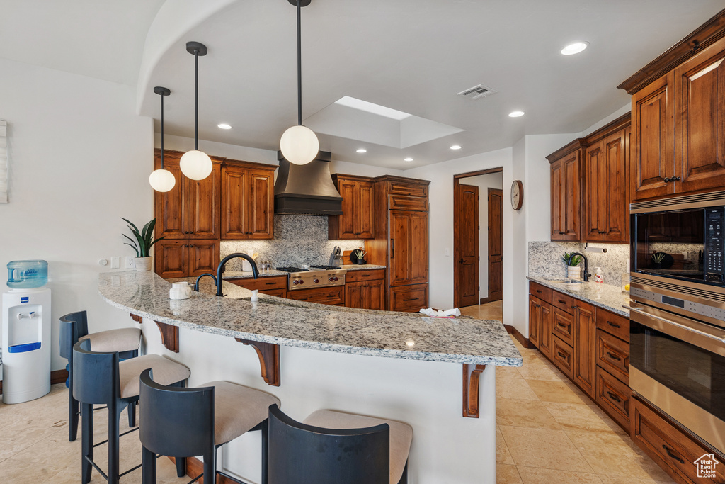 Kitchen with hanging light fixtures, custom exhaust hood, stainless steel appliances, and backsplash