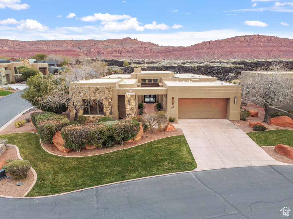 Pueblo revival-style home with a front lawn, a garage, and a mountain view