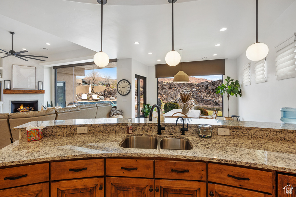 Kitchen with decorative light fixtures, light stone counters, ceiling fan, and sink