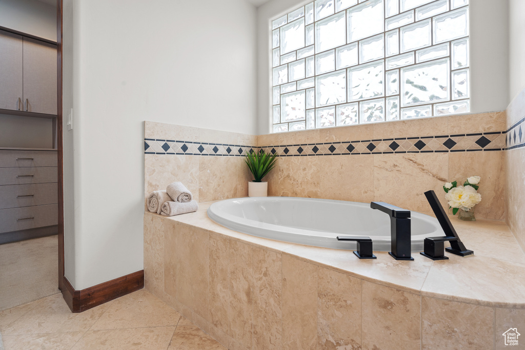 Bathroom featuring a wealth of natural light, a relaxing tiled bath, and tile flooring