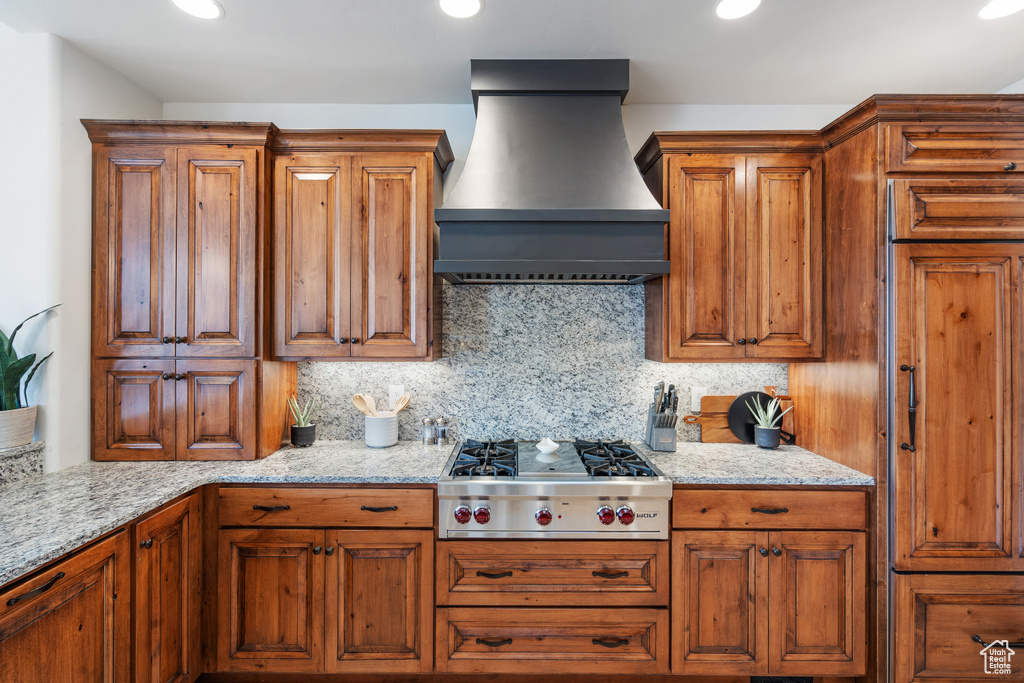 Kitchen with custom range hood, light stone counters, stainless steel gas stovetop, and tasteful backsplash