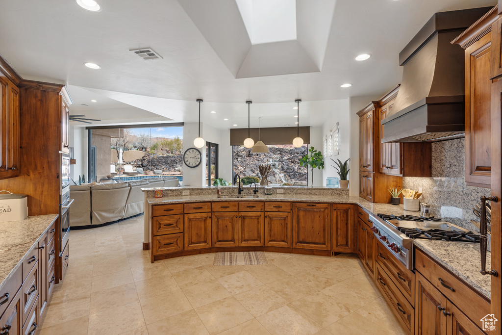Kitchen with light tile flooring, light stone counters, custom range hood, and stainless steel gas cooktop