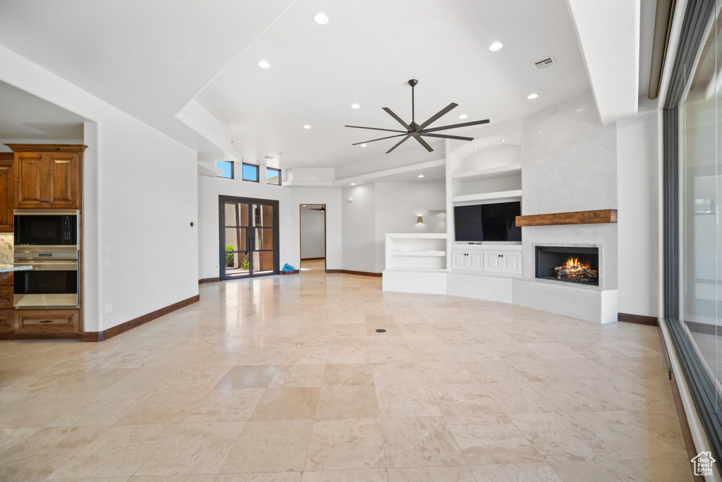 Unfurnished living room with a large fireplace, light tile flooring, built in features, a towering ceiling, and ceiling fan