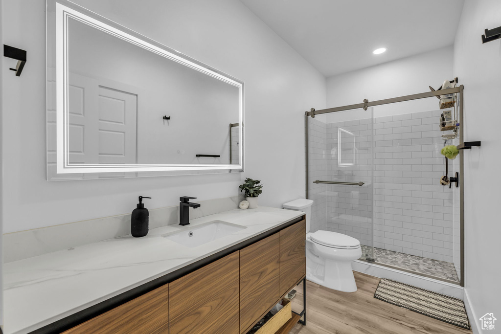 Bathroom featuring a shower with door, hardwood / wood-style flooring, toilet, and vanity with extensive cabinet space
