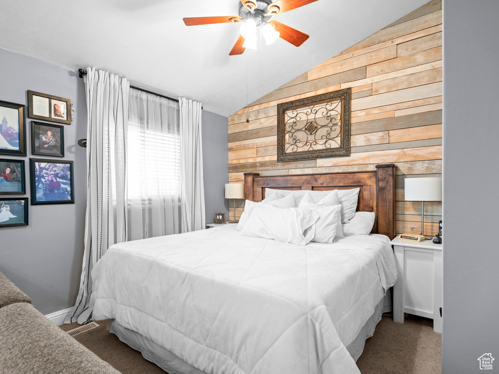 Carpeted bedroom with lofted ceiling, ceiling fan, and wood walls