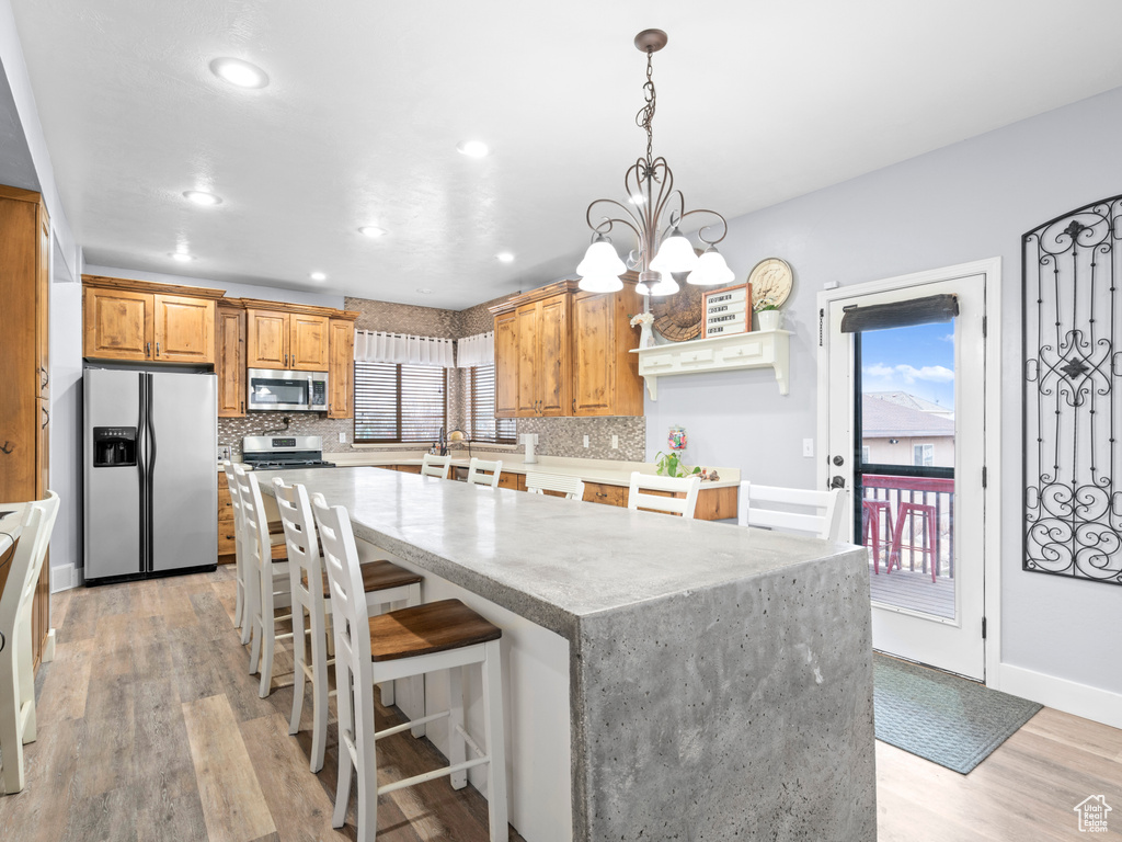 Kitchen with appliances with stainless steel finishes, decorative light fixtures, light hardwood / wood-style floors, and backsplash