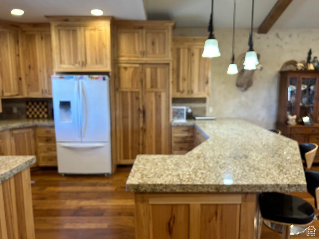 Kitchen featuring pendant lighting, white fridge with ice dispenser, and light stone counters