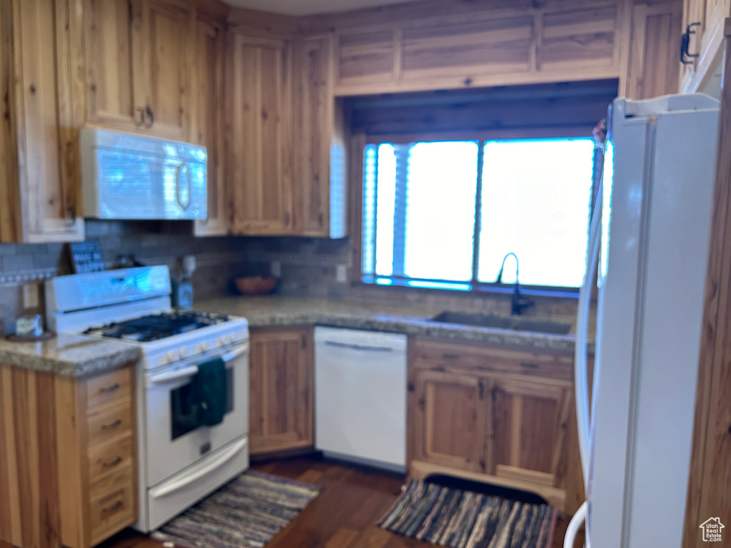 Kitchen featuring white appliances, dark hardwood / wood-style floors, backsplash, and sink