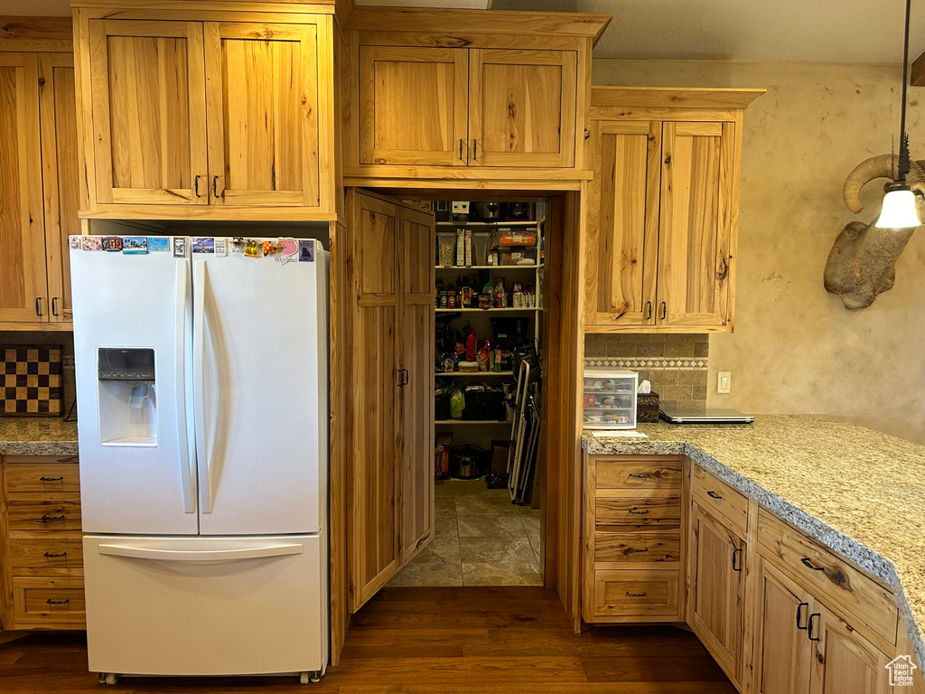 Kitchen with tasteful backsplash, light stone countertops, white fridge with ice dispenser, and dark tile flooring