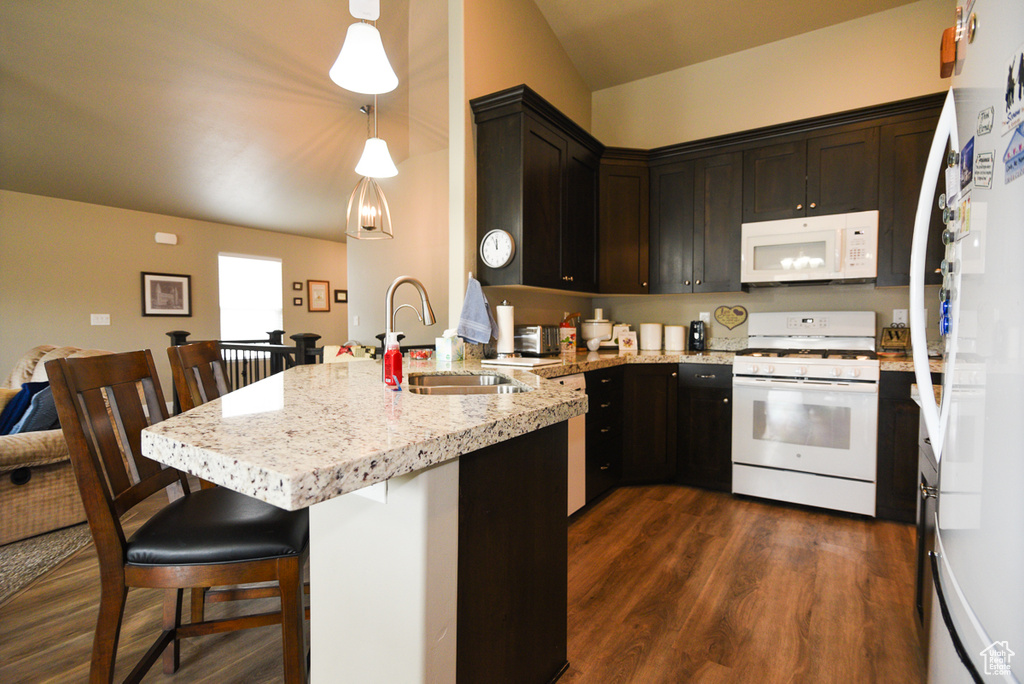 Kitchen with a kitchen bar, dark hardwood / wood-style flooring, sink, white appliances, and pendant lighting