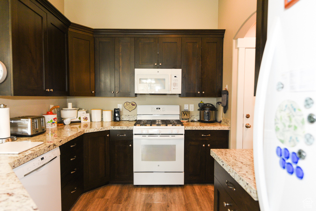 Kitchen featuring white appliances, light hardwood / wood-style floors, dark brown cabinetry, and light stone counters