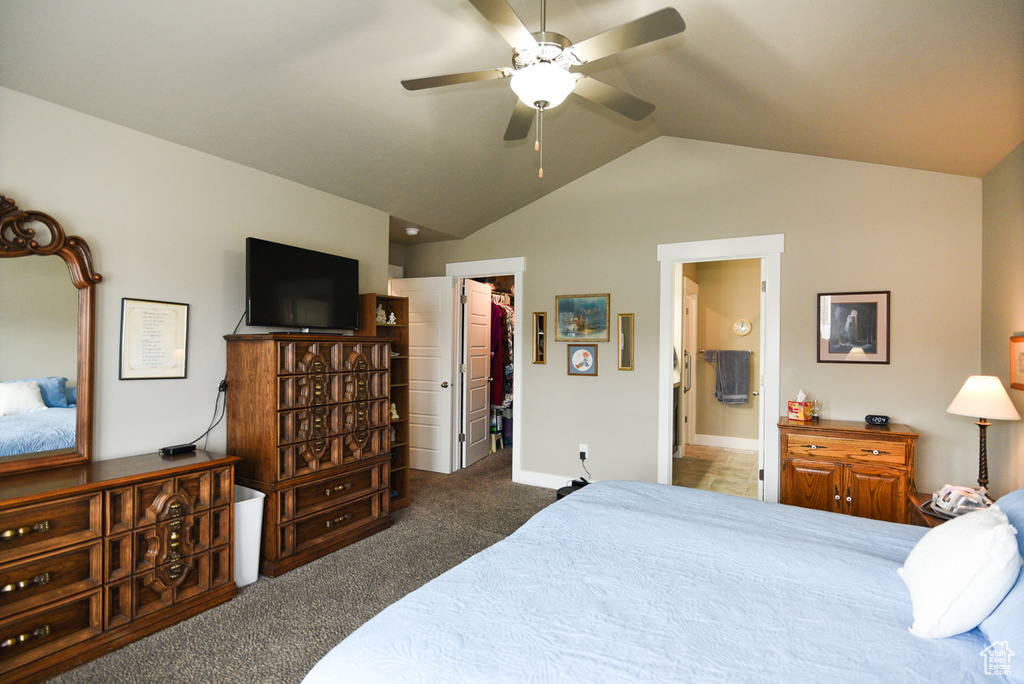 Carpeted bedroom featuring ceiling fan, vaulted ceiling, a closet, a walk in closet, and ensuite bathroom