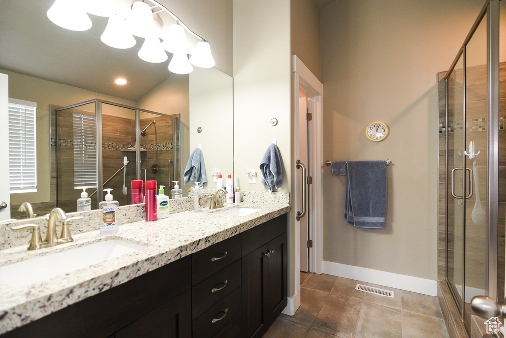 Bathroom featuring dual sinks, an enclosed shower, tile floors, and vanity with extensive cabinet space