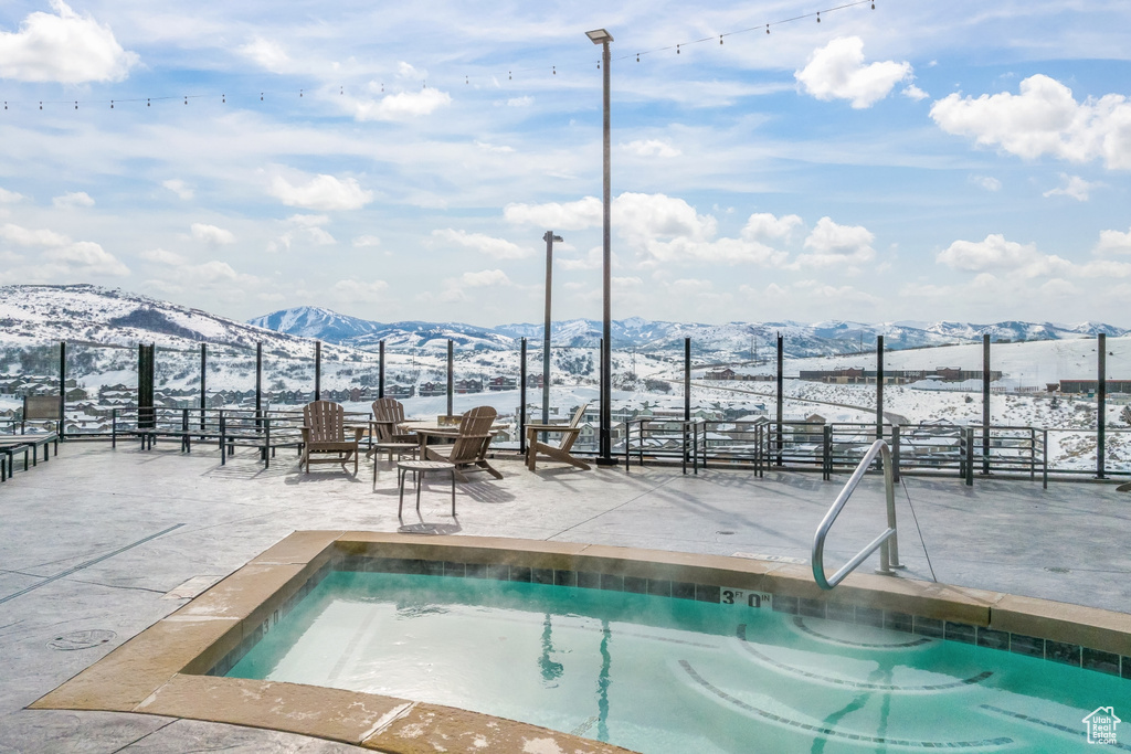 Snow covered pool featuring a hot tub and a mountain view