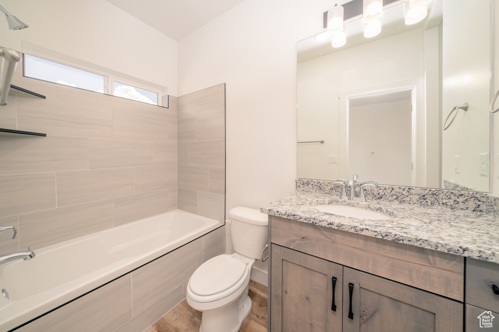 Full bathroom featuring hardwood / wood-style flooring, tiled shower / bath combo, oversized vanity, and toilet