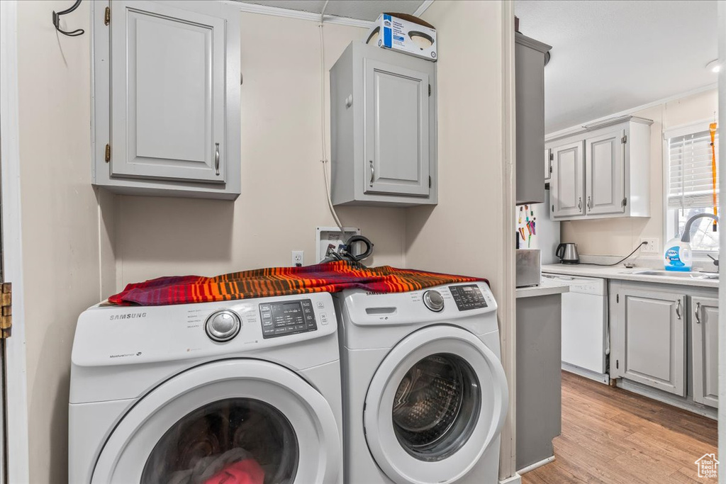 Laundry area with light hardwood / wood-style flooring, independent washer and dryer, cabinets, crown molding, and sink