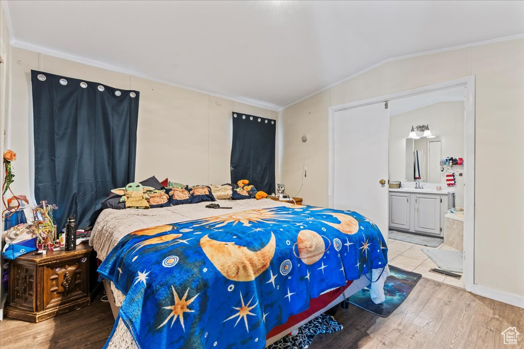Bedroom featuring ensuite bath, light hardwood / wood-style flooring, vaulted ceiling, and ornamental molding