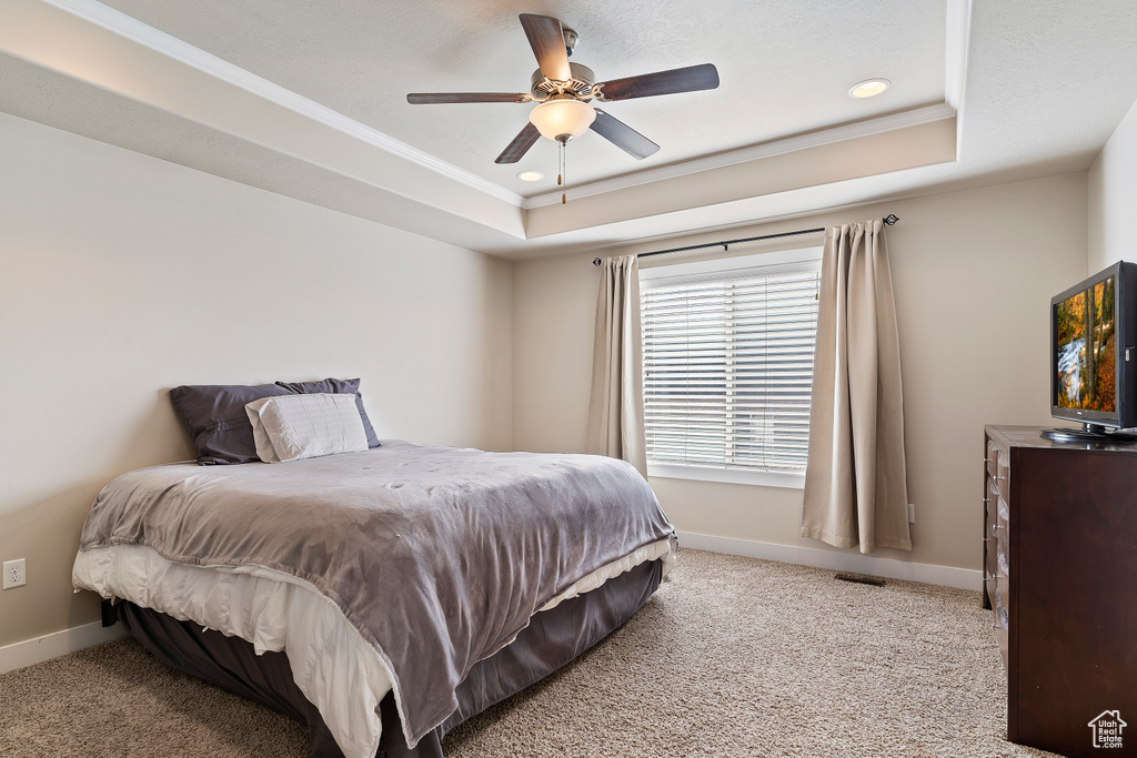 Bedroom featuring ceiling fan, light colored carpet, a tray ceiling, and ornamental molding