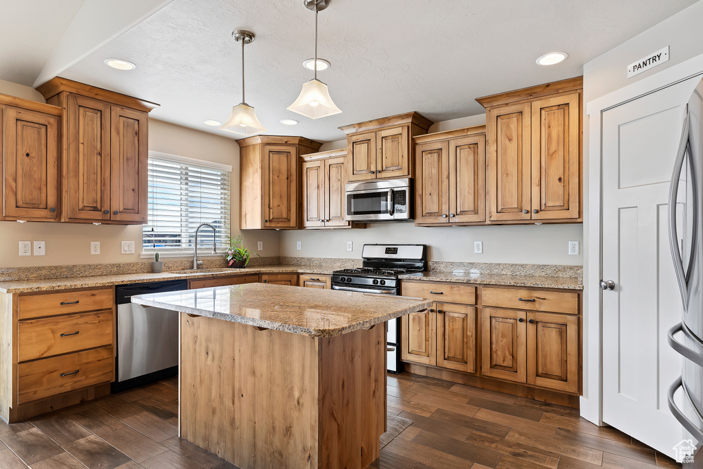 Kitchen with a kitchen island, light stone countertops, dark hardwood / wood-style floors, stainless steel appliances, and pendant lighting