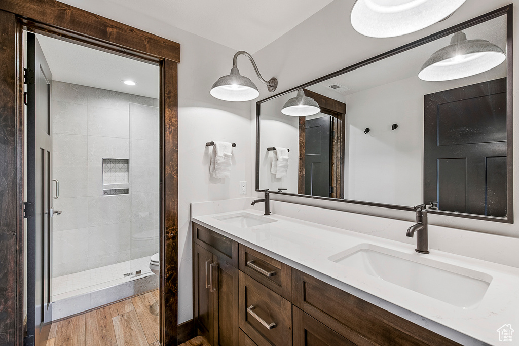 Bathroom with hardwood / wood-style flooring, double sink vanity, walk in shower, and toilet