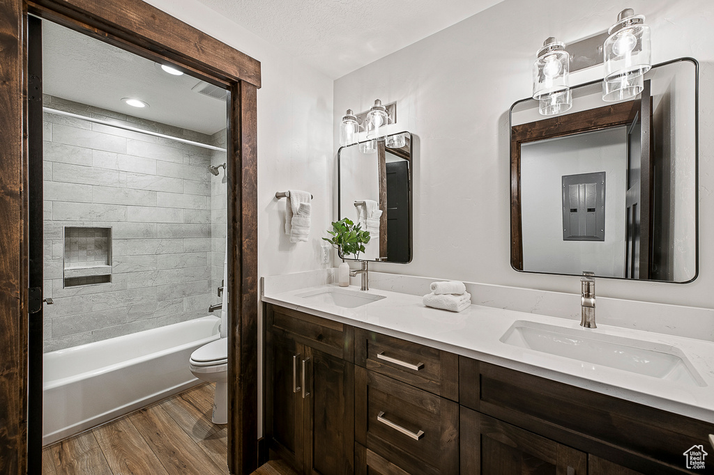 Full bathroom featuring a textured ceiling, tiled shower / bath combo, hardwood / wood-style flooring, toilet, and dual bowl vanity