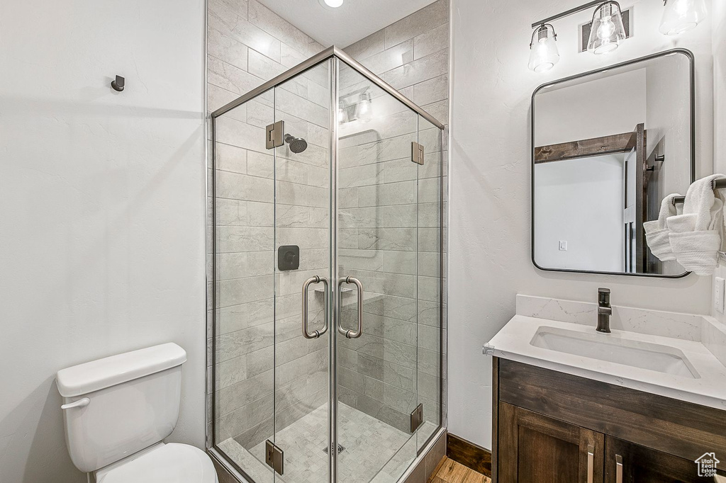 Bathroom with hardwood / wood-style floors, a shower with door, vanity, and toilet
